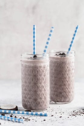 A couple of glasses of light oreo smoothie with blue and white striped straws in them