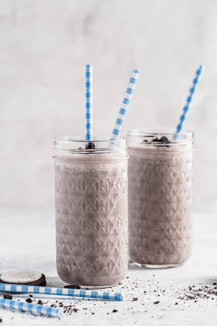 A couple of glasses of oreo milkshake with blue and white striped straws in them