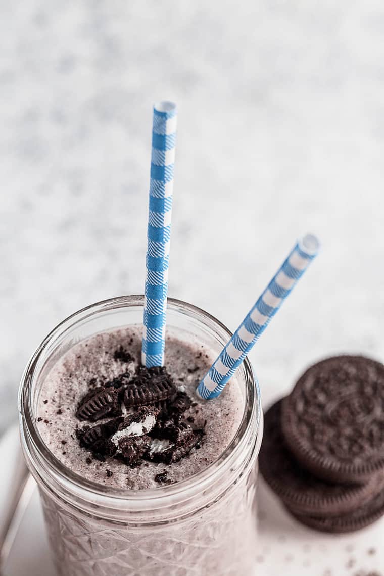 Overhead shot of a glass of oreo milkshakes with two blue and white striped straws and a few oreo cookies stacked on top of each other next to it