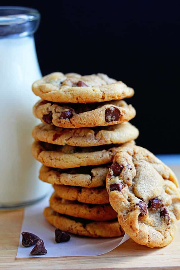 Close up of a stack of chewy chocolate chip cookies next to a jug of milk