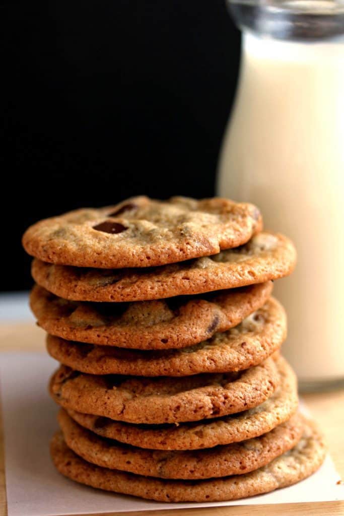 Close up of a stack of crispy chocolate chip cookies next to a jug of milk
