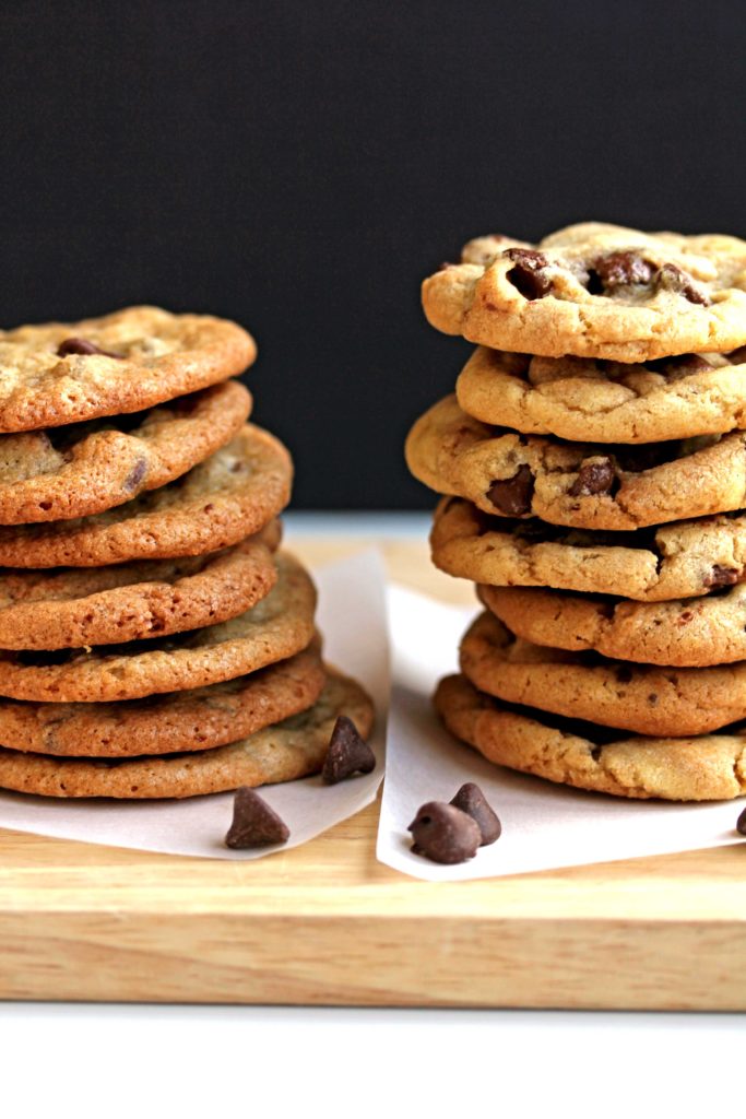 A stack of crispy chocolate chip cookies on the left and a stack of chewy chocolate chip cookies on the right sitting on parchment paper