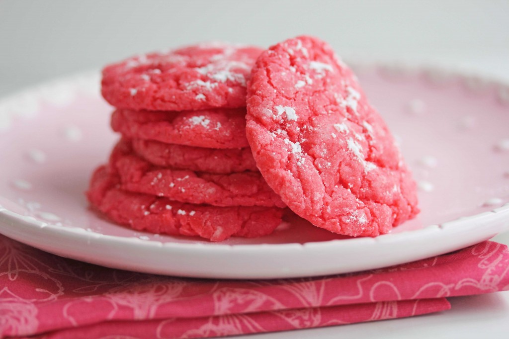 A stack of raspberry gooey butter cookies topped with powdered sugar and sitting on a round, pink plate on top of a pink cloth