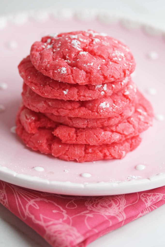 Close up of a stack of raspberry gooey butter cookies topped with powdered sugar and sitting on a round, pink plate on top of a pink cloth