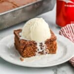 A square of coca cola cake with a scoop of ice cream on the table in front of the pan.