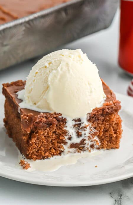 A square of coca cola cake with a scoop of ice cream on the table in front of the pan.