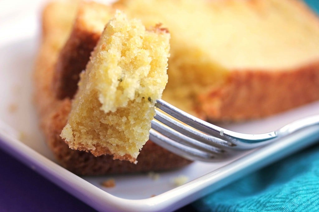 Close up of a small piece of cornmeal pound cake on a fork with two slices of the cake in the background and out of focus