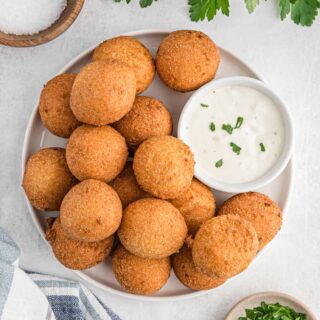 A plate of hush puppies with a sauce on a white background