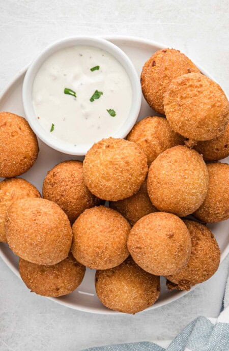 A plate of southern hush puppies with a small bowl of sauce.