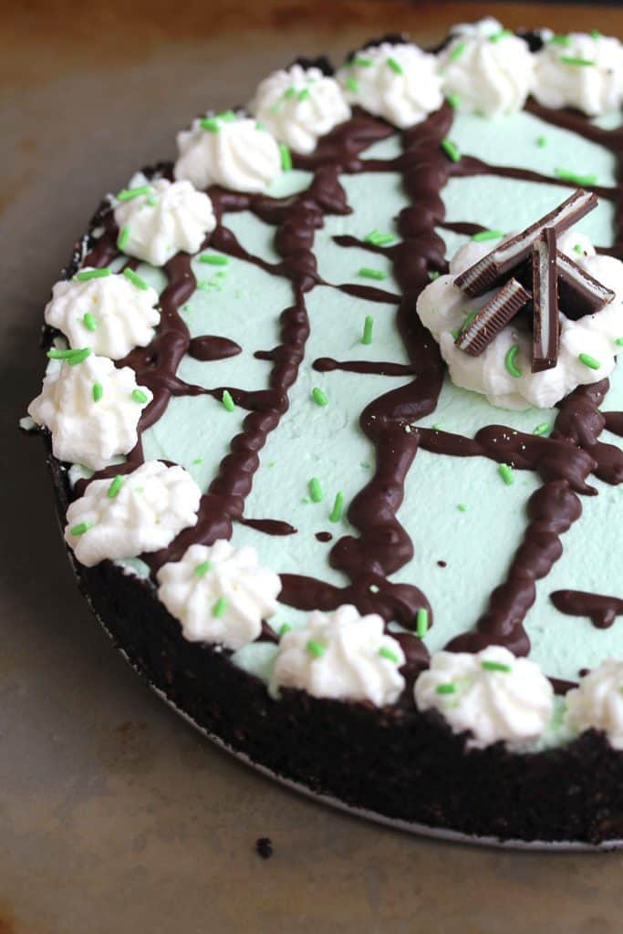 A mint chocolate pie with chocolate drizzle and whipped cream ready to cut into