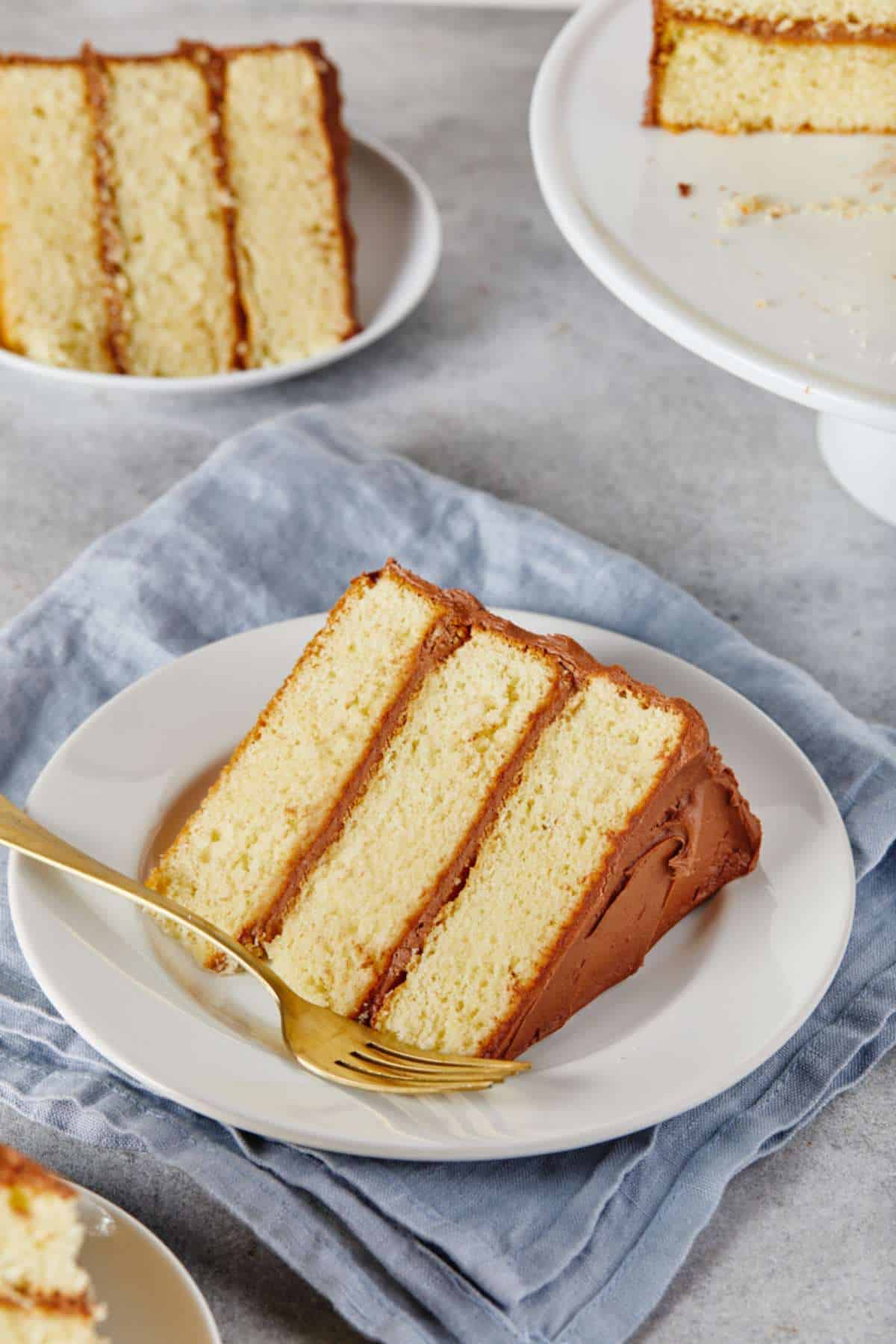 Yellow Cake Recipe with Chocolate Frosting slices on white plates on a gray background