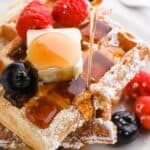 buttermilk waffles on a white plate with syrup pouring down with butter on top and berries