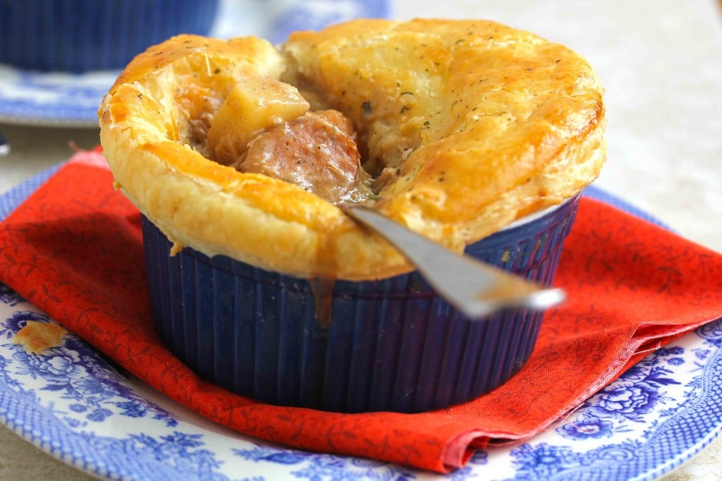 Creole pot pie in a small blue bowl with a spoon in it holding sausage and a piece of potato