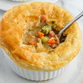 A chicken and sausage pot pie with a spoon breaking the crust to show the filling inside.