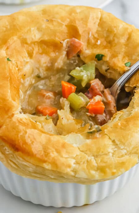 A chicken and sausage pot pie with a spoon breaking the crust to show the filling inside.