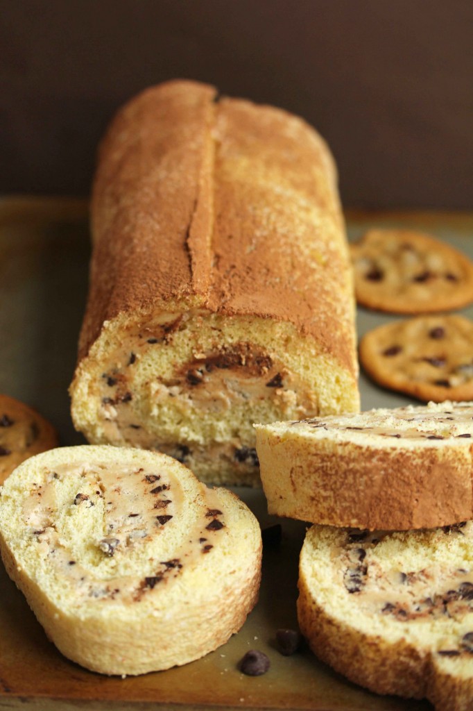 Cookie dough cake roll with three pieces cut out of it and three crispy chocolate chip cookies next to it