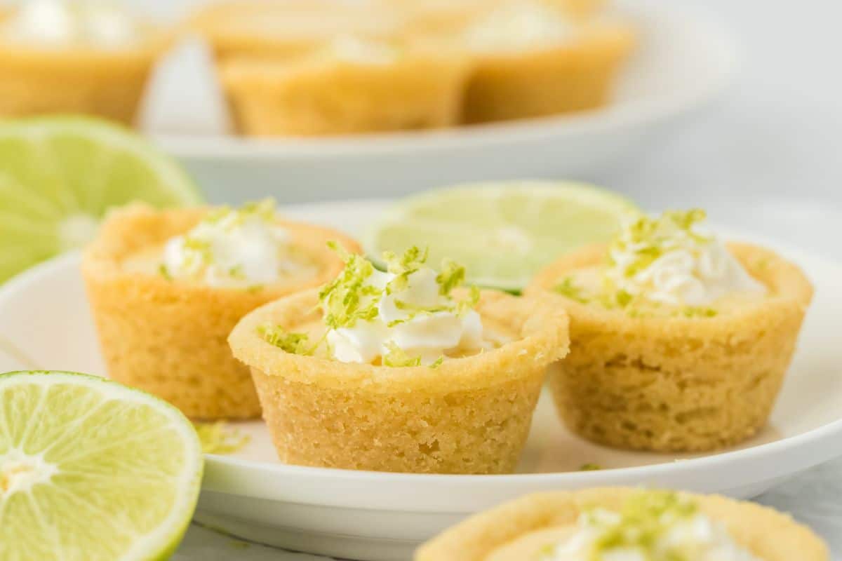 A plate with three key lime cookie cups on it and lime halves and slices around on the table.
