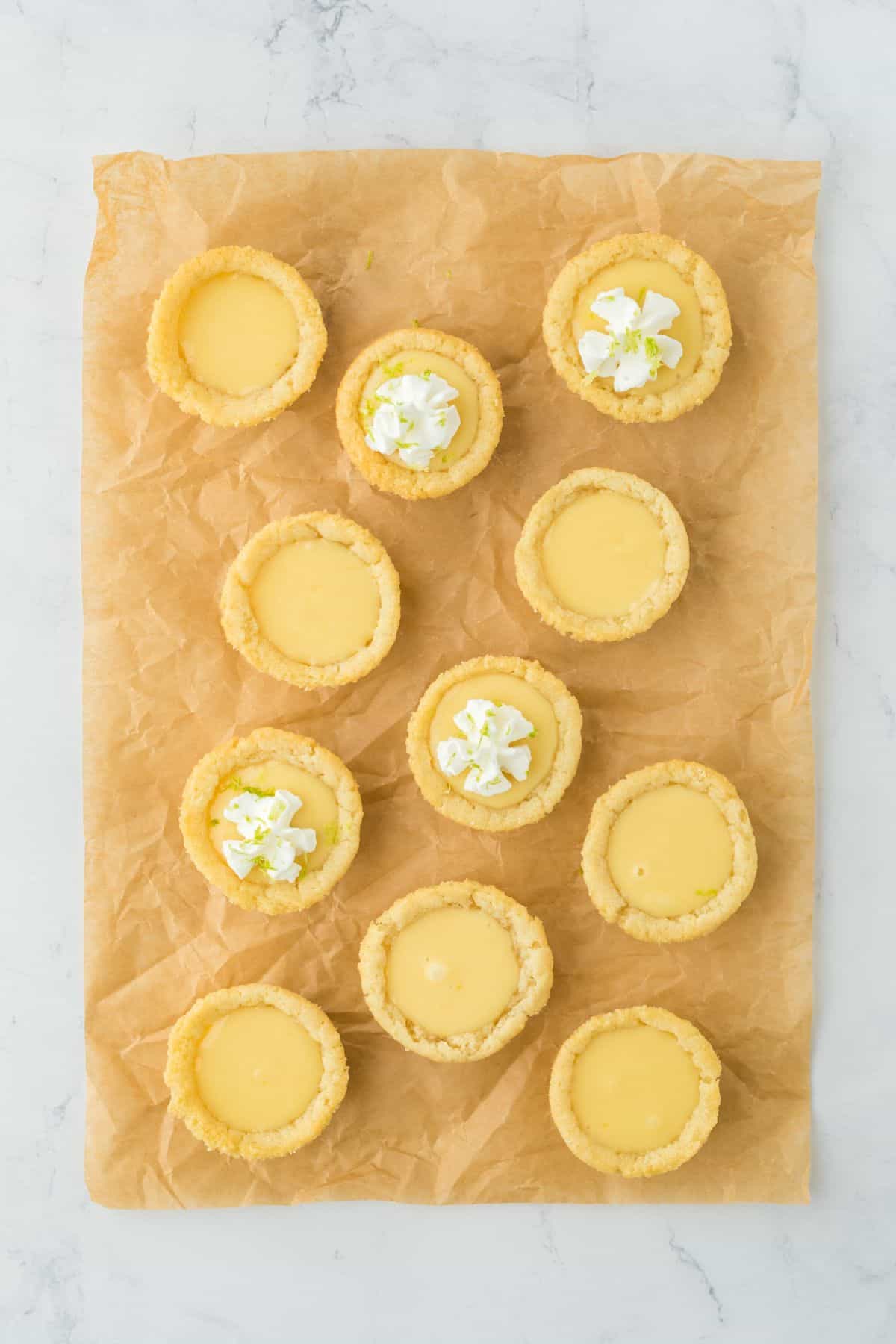 Key lime cookie cups on a piece of parchment some are topped with whipped cream.