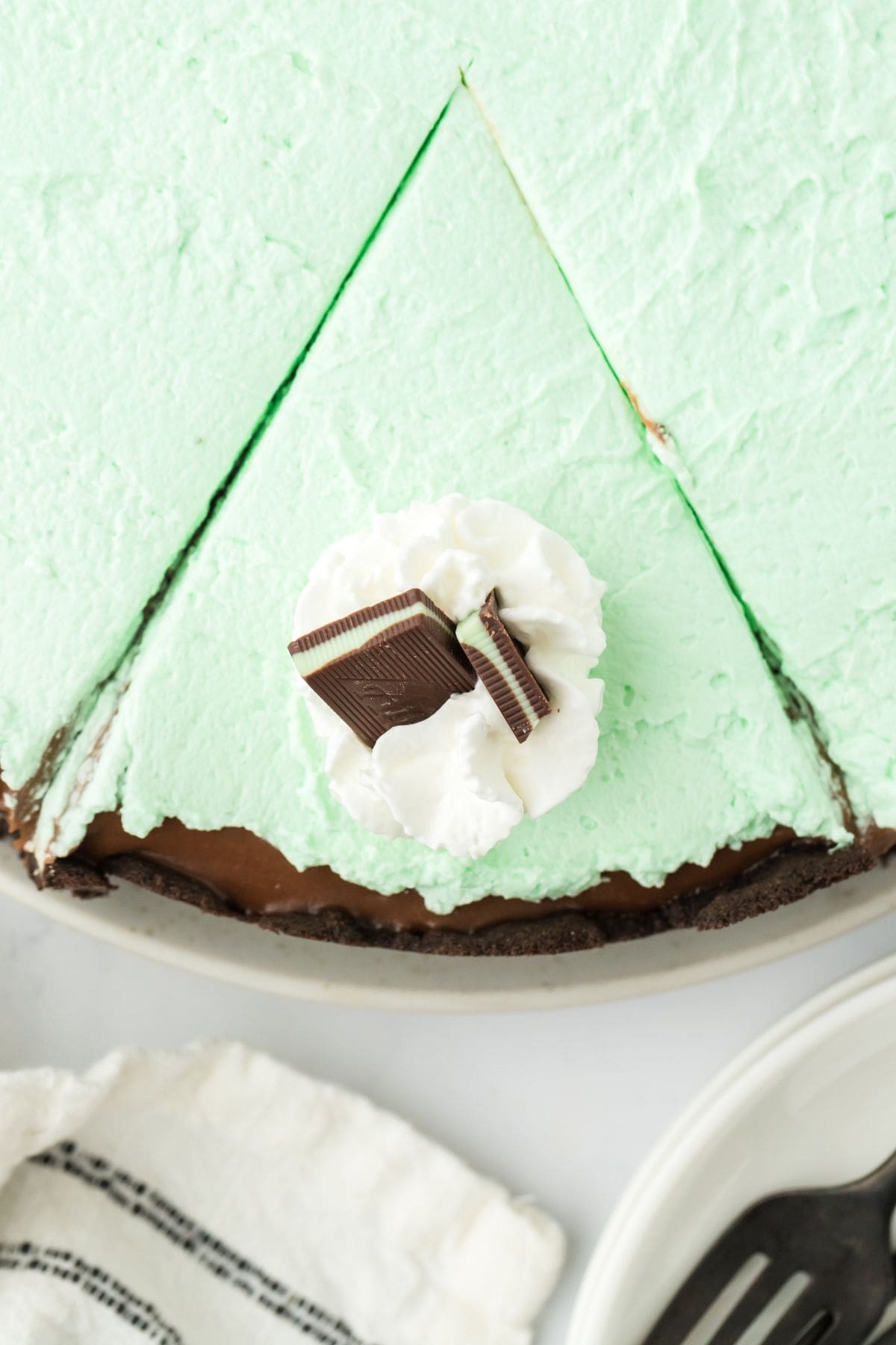 Mint chocolate cream pie with a slice cut and topped with whipped cream and mint candy.