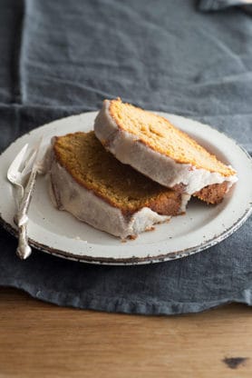 Two slices of sweet potato cake stacked on top of each other sitting on a round, white plate next to a knife and fork