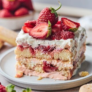 A square of strawberry tiramisu on a plate with fresh berries on top.