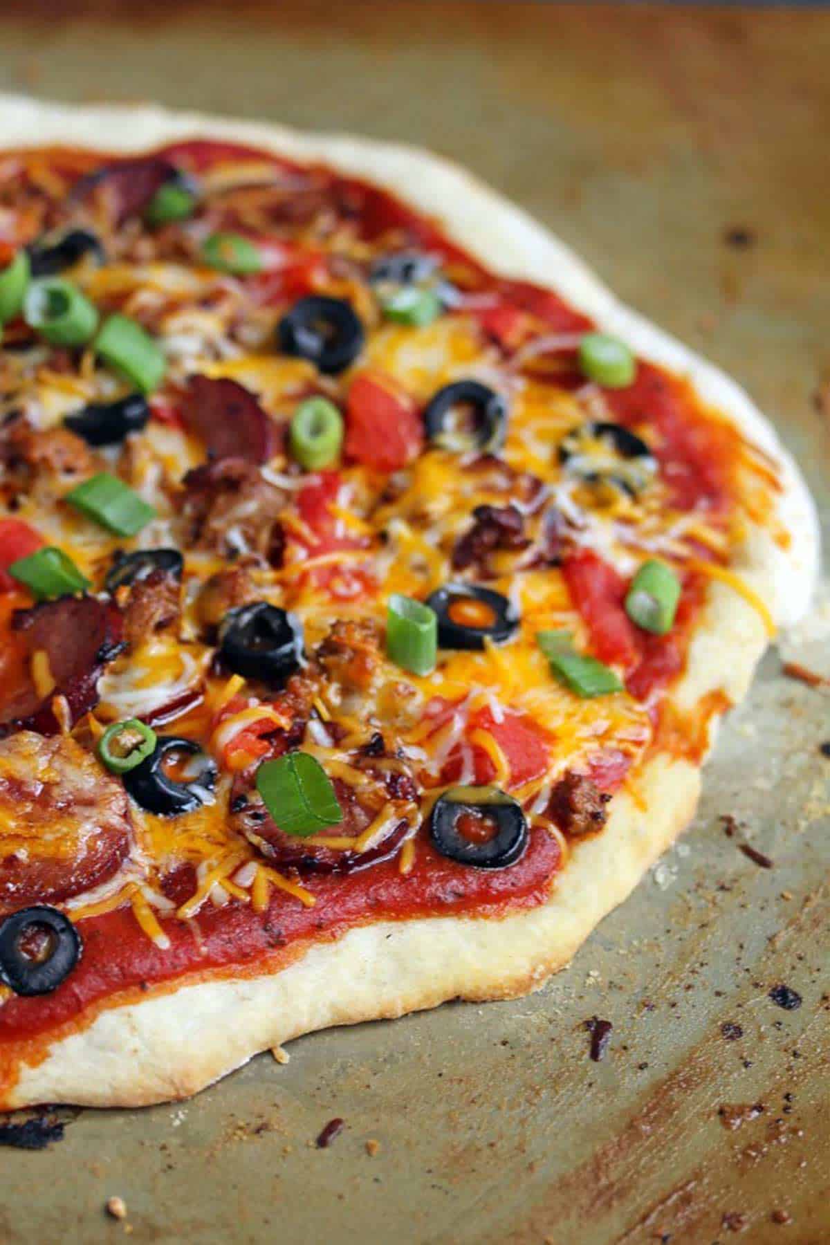 Half a Mexican pizza topped with chorizo sausage, green peppers, black olives and diced tomatoes on a baking pan.