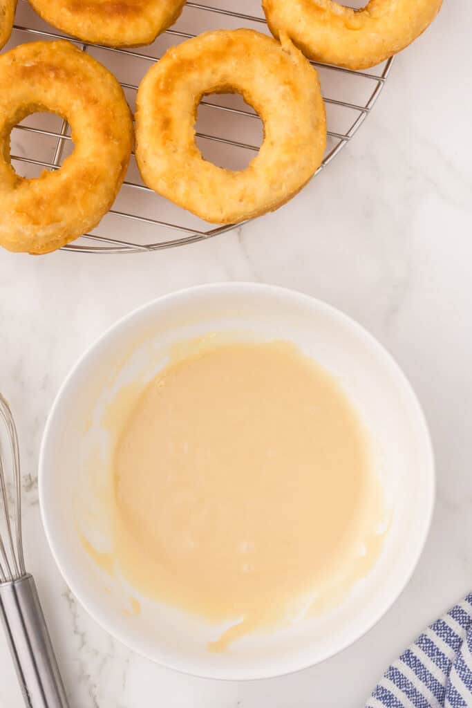 Prepared maple glaze in a bowl next to the fried doughnuts