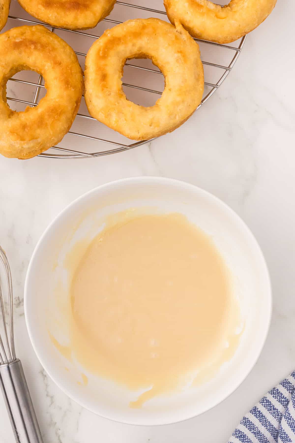Prepared maple glaze in a bowl next to the fried doughnuts