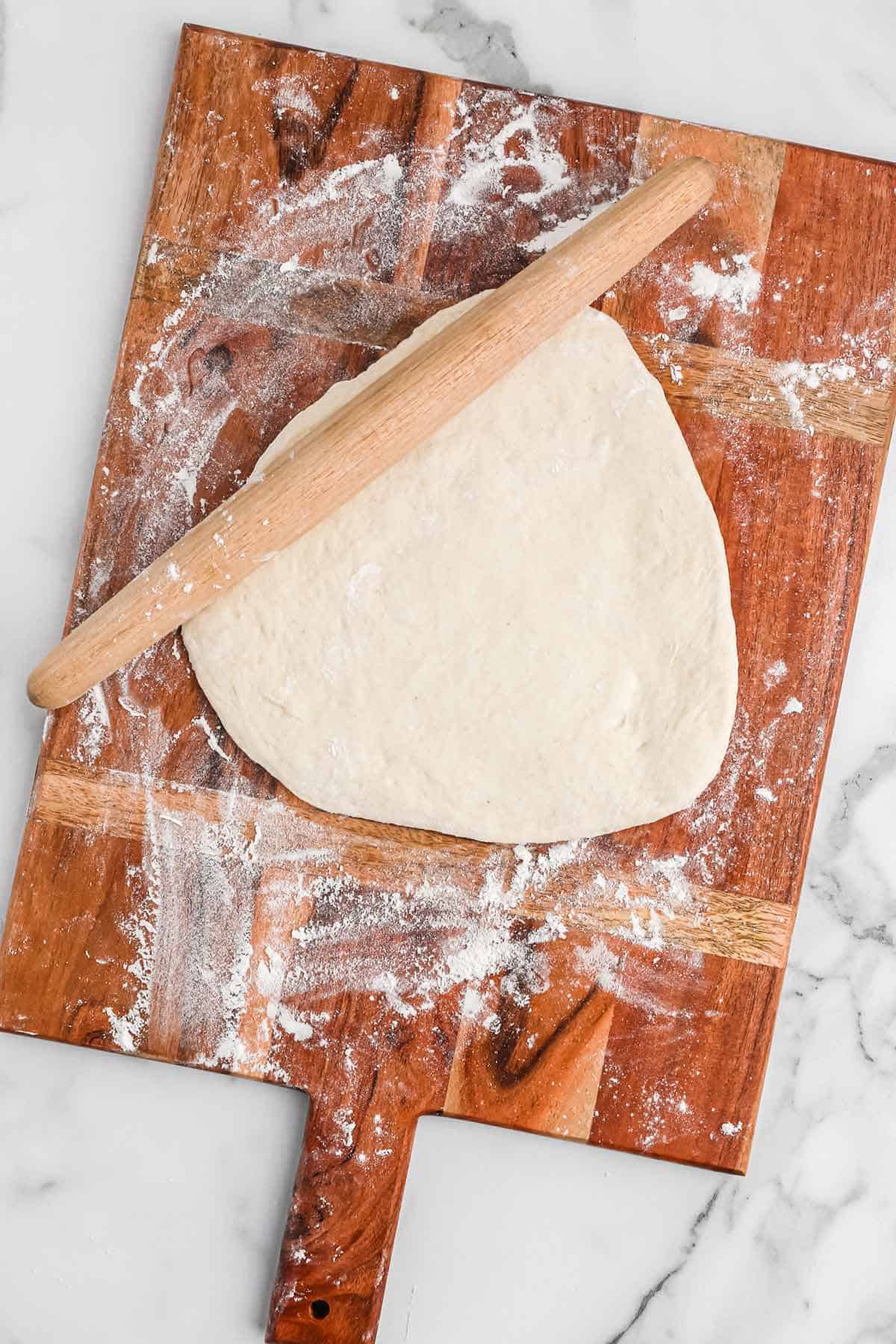 Pizza dough rolled out on a cutting board with rolling pin.