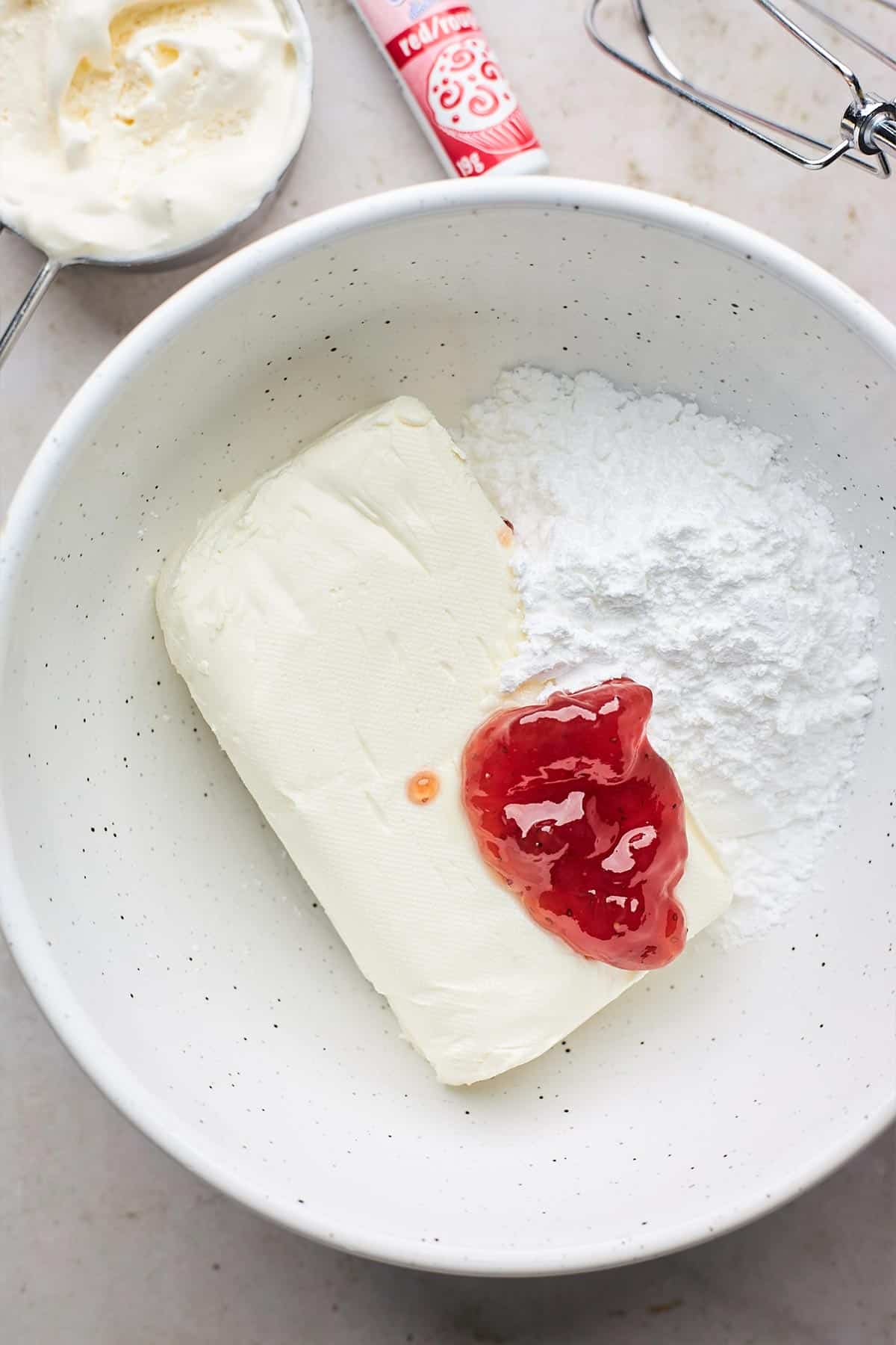 Powdered sugar, cream cheese, and strawberry in a mixing bowl.
