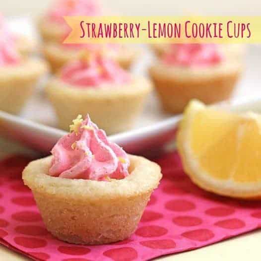 Close up of one strawberry lemon cookie cup with a lemon wedge next to it and more cookie cups in the background and out of focus