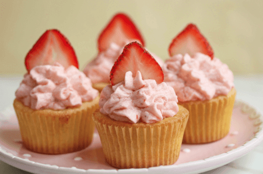Close up of strawberry lemonade cupcakes on a pink plate and topped with one fresh sliced strawberry