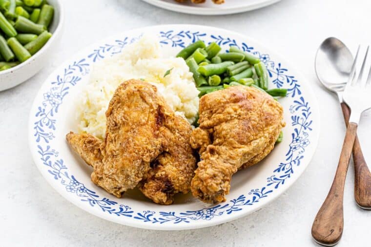 A plate on the table with fried chicken, mashed potatoes, and green beans.