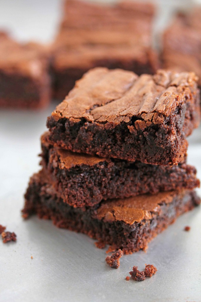 Three chewy brownies stacked on top of each other with more brownies in the background