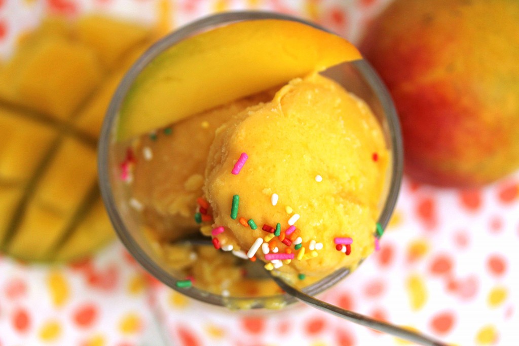 Overhead shot of a couple of scoops of mango frozen yogurt in a glass topped with sprinkles and spoon in it