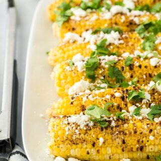 A platter of Mexican grilled corn with limes in the background.