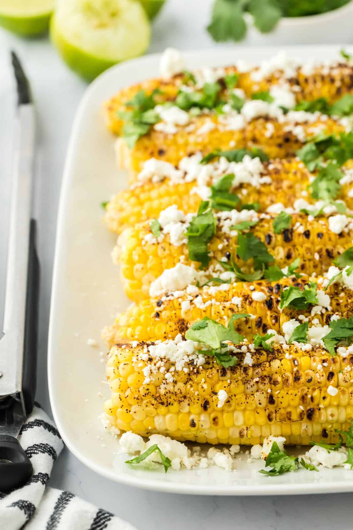 A platter of Mexican grilled corn with limes in the background.