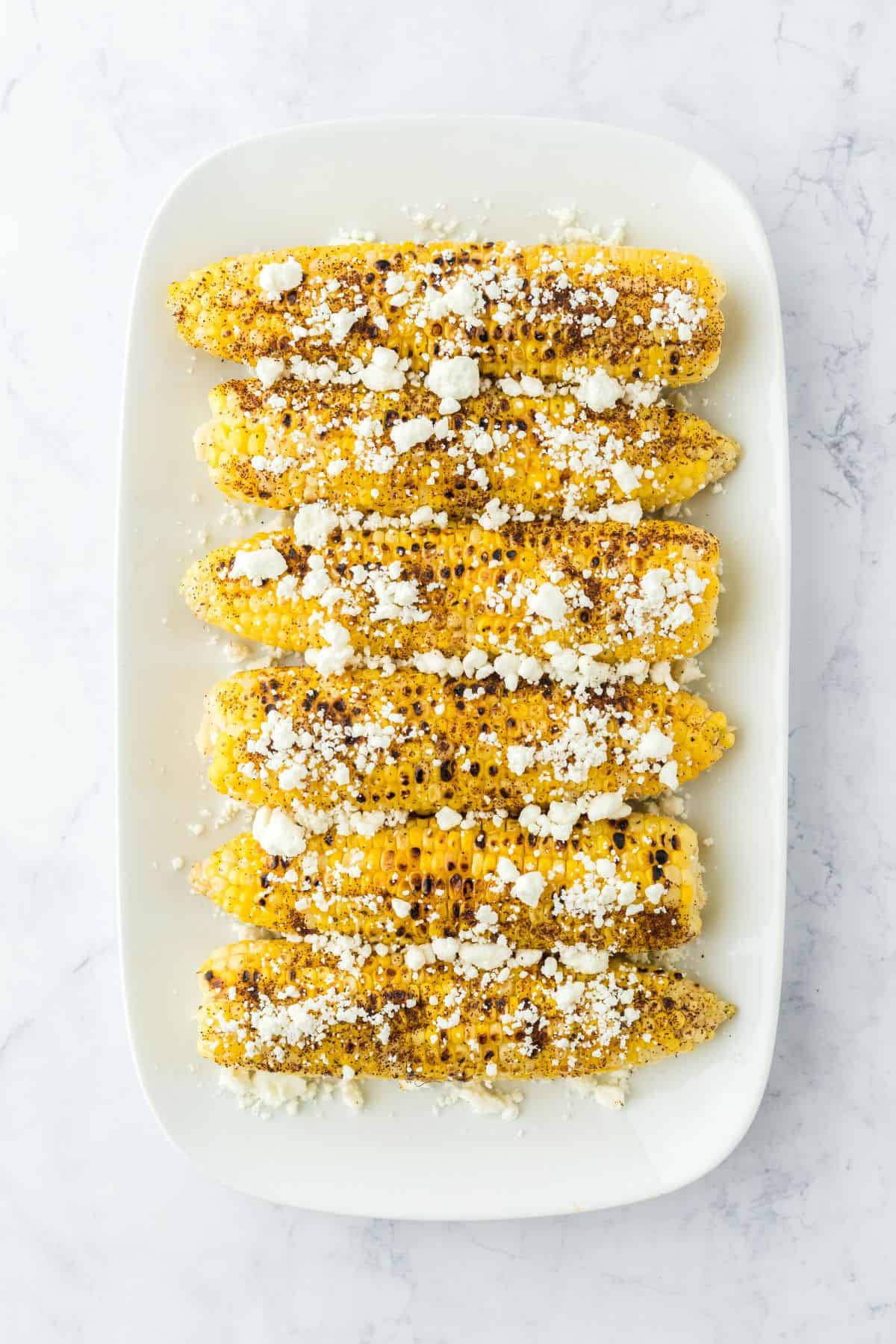A platter of Mexican grilled corn on a platter topped with cheese.