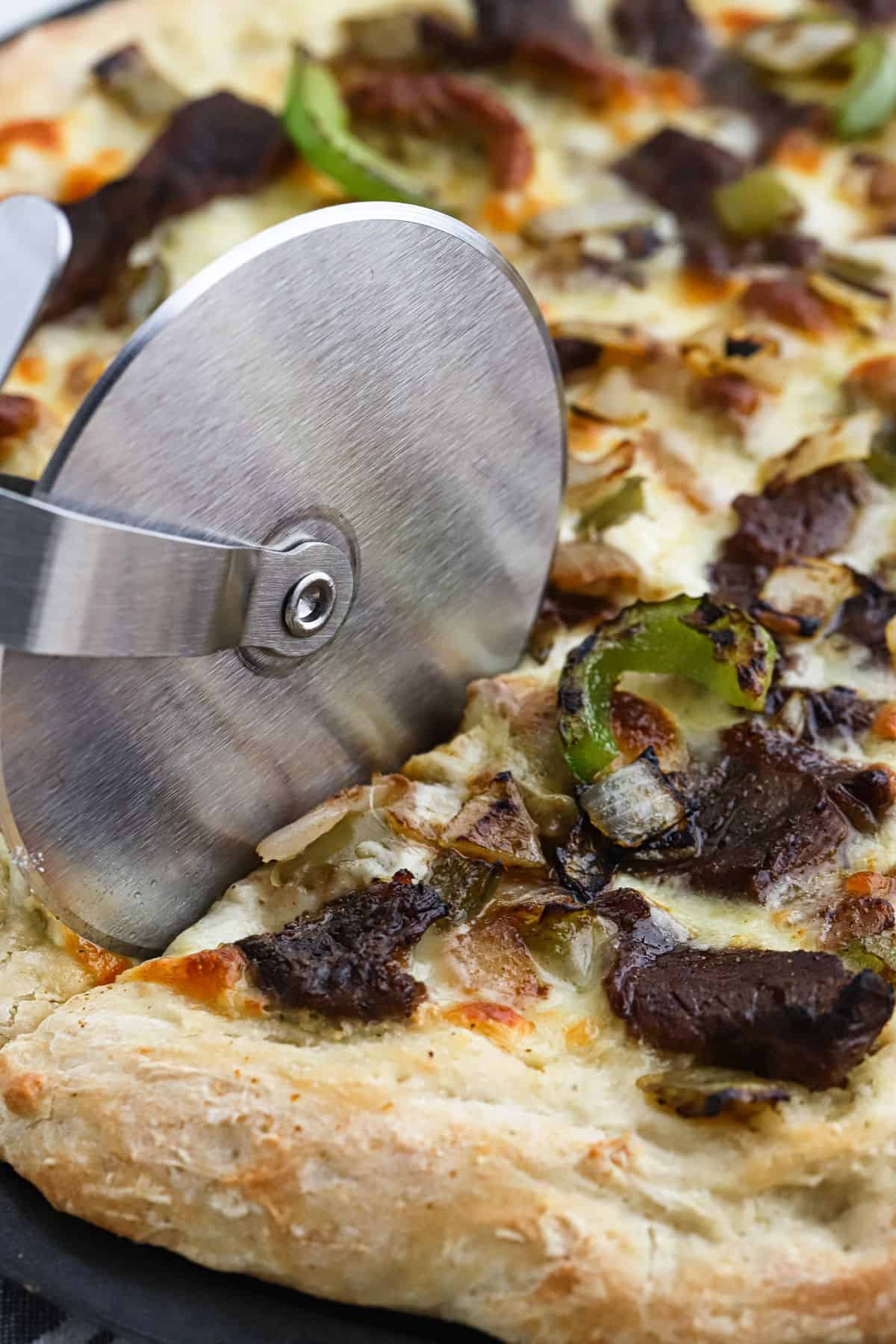 A pizza wheel slicing a piece of steak pizza.