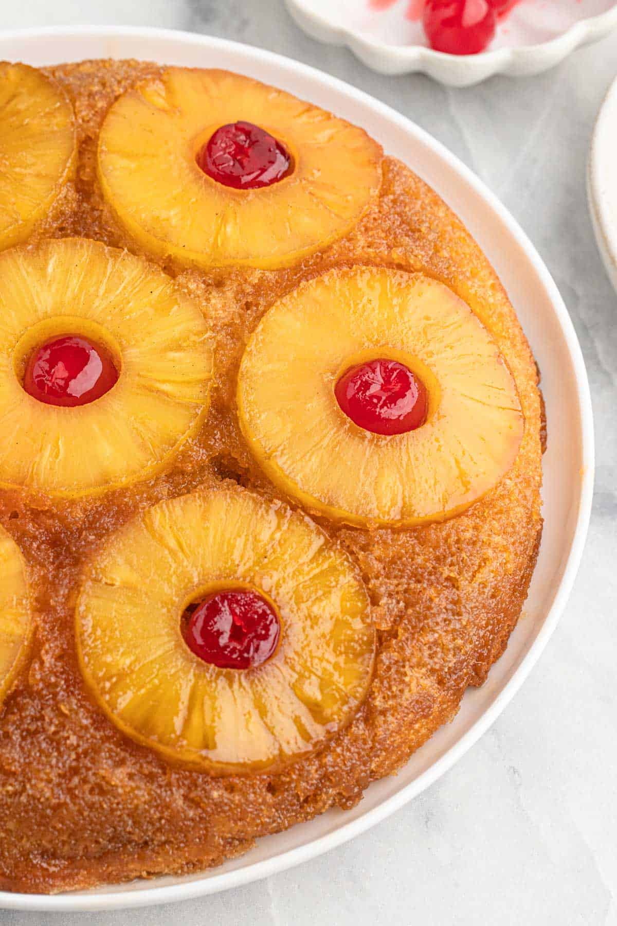 A pineapple upside down cake on a white platter with rings of caramelized pineapple rings and cherries.