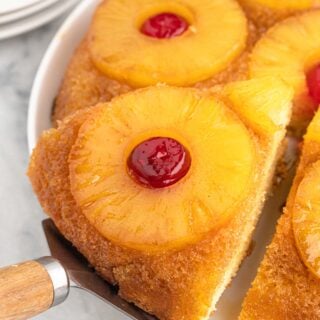 A slice of pineapple upside down cake being taken out of a cake on a white background
