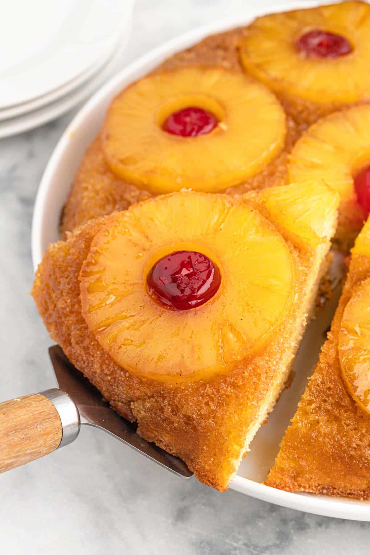 A pineapple cake with pineapple rings and cherries on top with a spatula lifting out a slice.