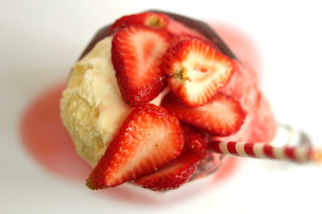 Overhead shot of a strawberry ice cream float contained in a glass mug with a red and white striped straw in it
