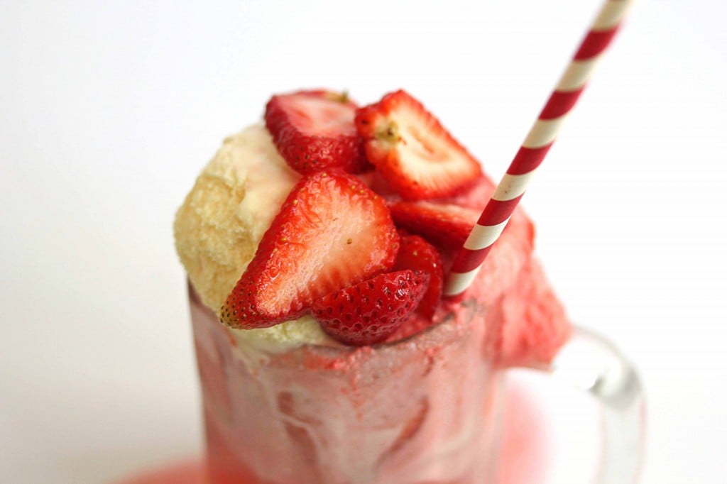 A strawberry ice cream float contained in a glass mug with a red and white striped straw in it