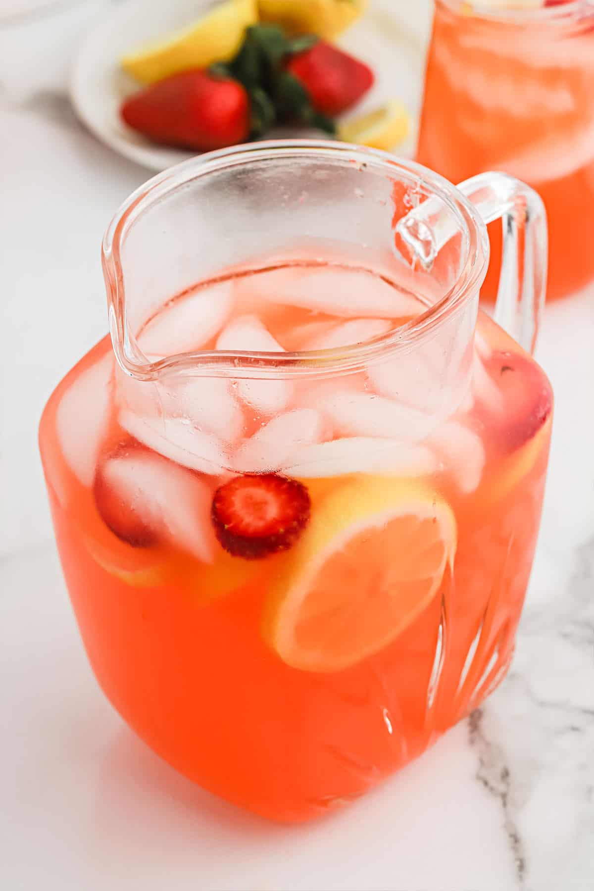A pitcher of strawberry lemonade with ice on the table.