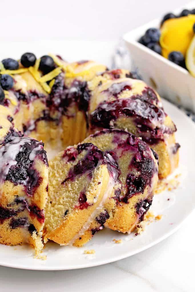Lemon Blueberry Pound Cake with slices cut out and placed on the same white plate the whole lemon blueberry cake is sitting on. It's a great blueberry pound cake.