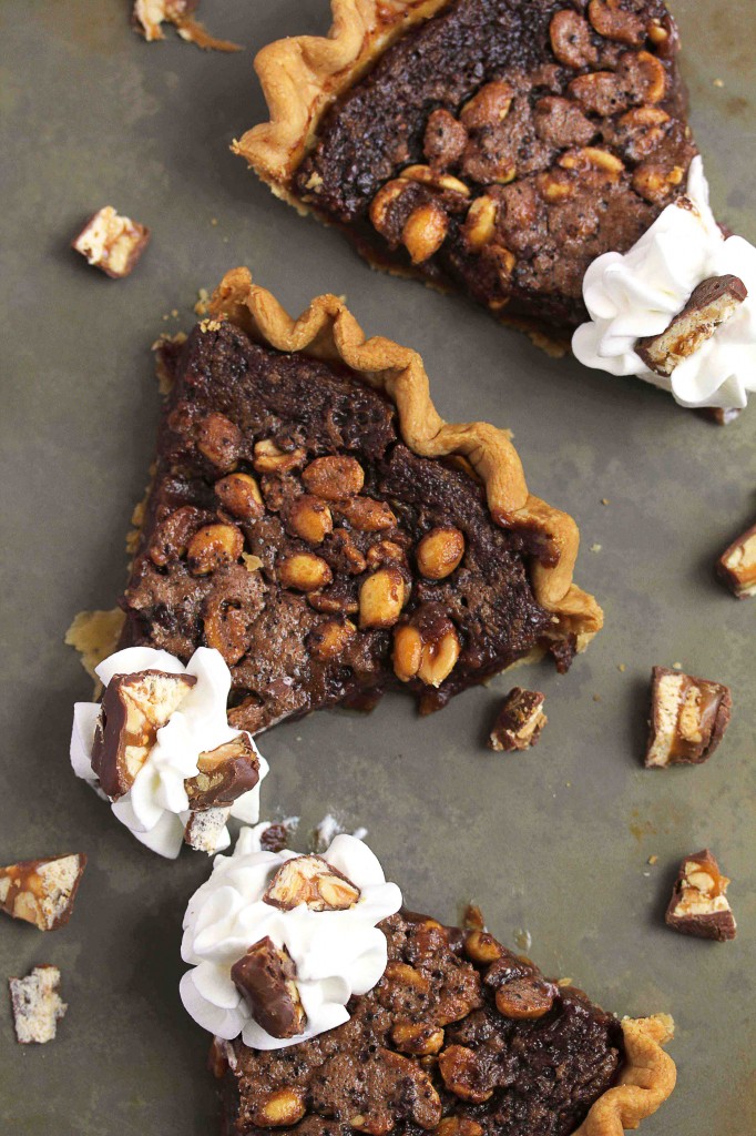 Overhead shot of three slices of fudge pie with pieces of candy bars scattered around them