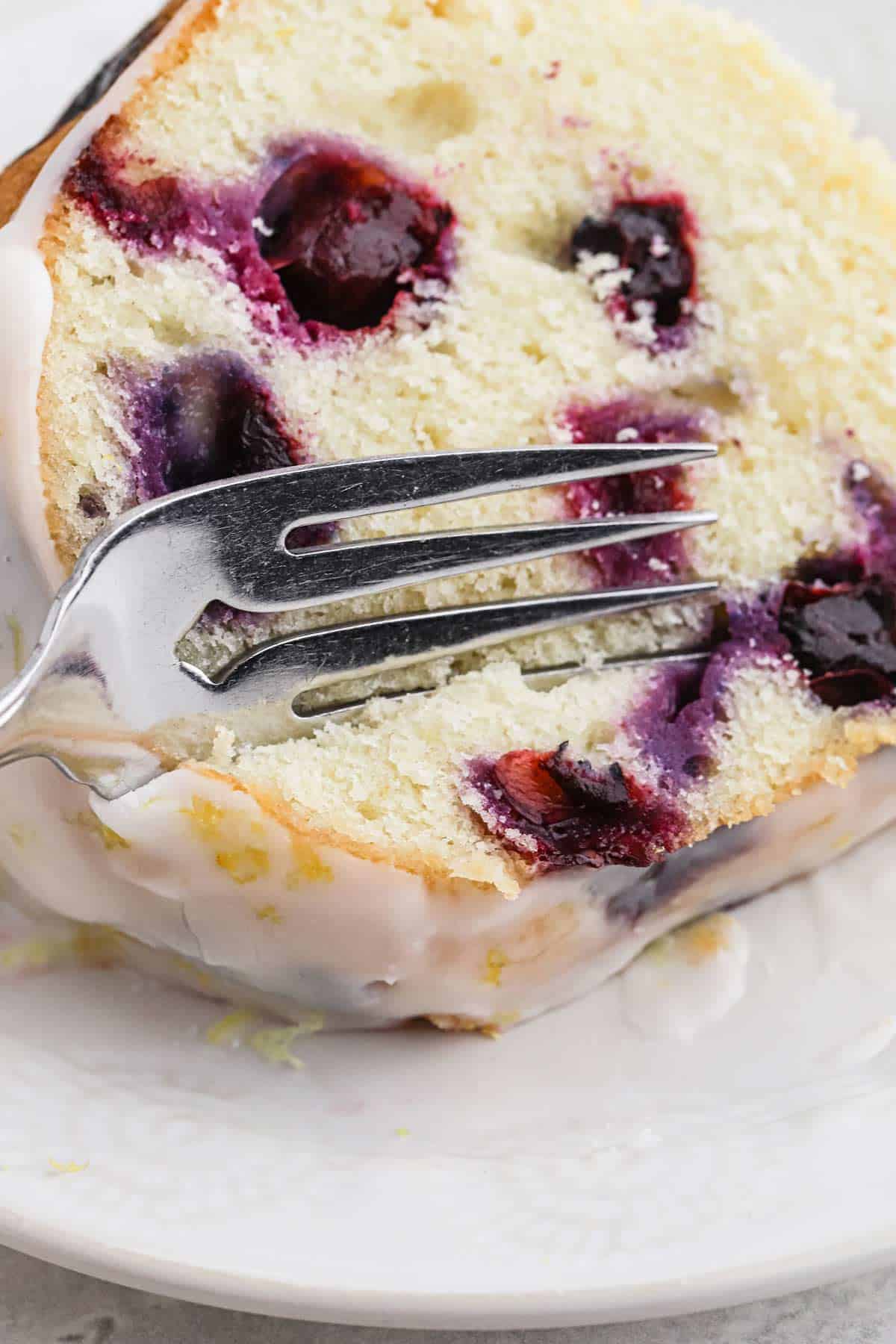A slice of lemon blueberry pound cake with a fork cutting a bite into it.
