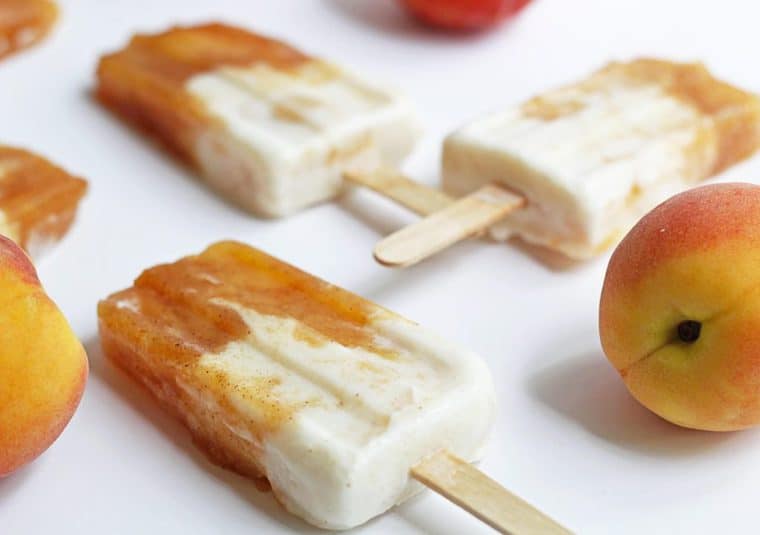 Three peaches and cream popsicles displayed with whole fresh peaches