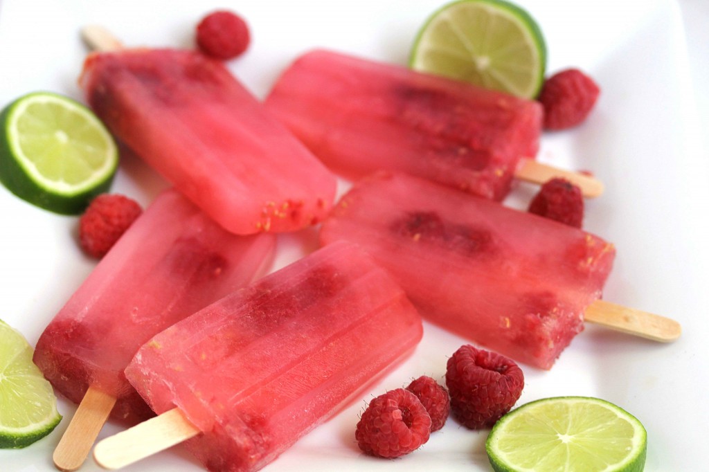 Five raspberry limeade popsicles surrounded by lime slices and fresh raspberries